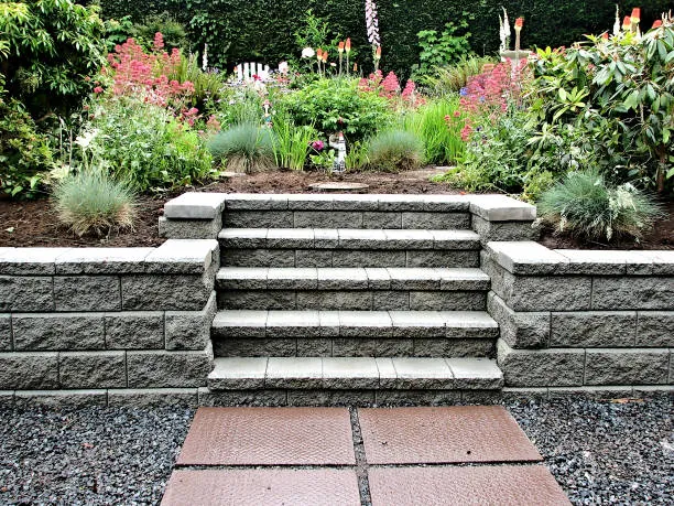 Wide block steps climbing between two block walls, with flowering shrubs and grasses on either side