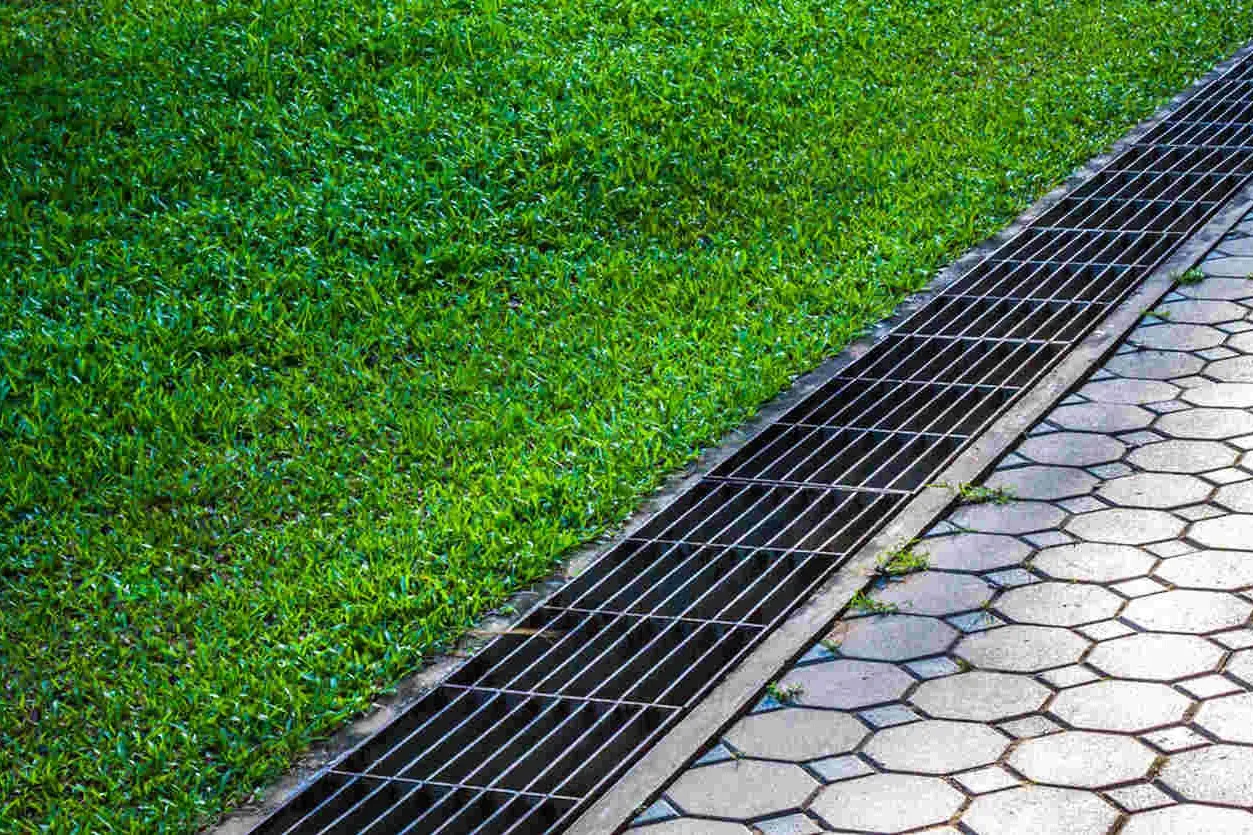 A grated channel drain set between a paver surface and a lawn