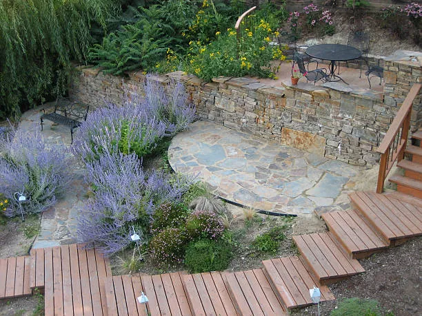 A flagstone terrace set into a slope, with lavender, stone walls and wooden steps down to a deck