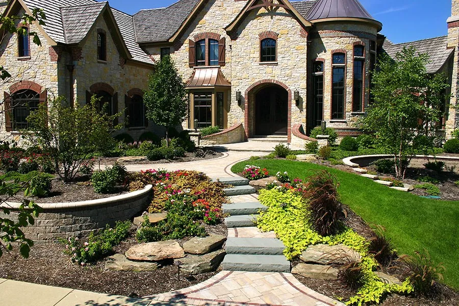 A stone house with layered front garden beds, boulders and a curving flagstone walk